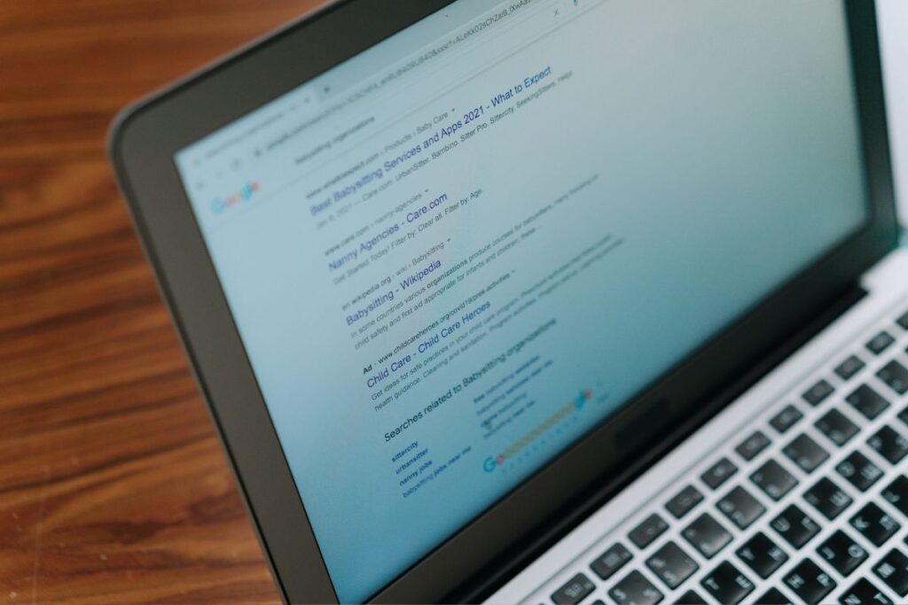 Tela de notebook mostrando os resultados de busca do Google para a frase "babysitting services". A imagem ilustra a otimização para mecanismos de busca, destacando o ranqueamento de sites.