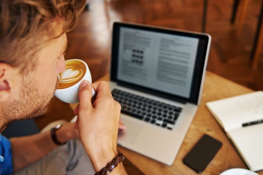 Homem tomando café enquanto usa ferramentas para blog em seu notebook.