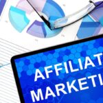 Laptop exibindo "Affiliate Marketing" com gráficos e relatórios de performance de plataforma de afiliados ao fundo