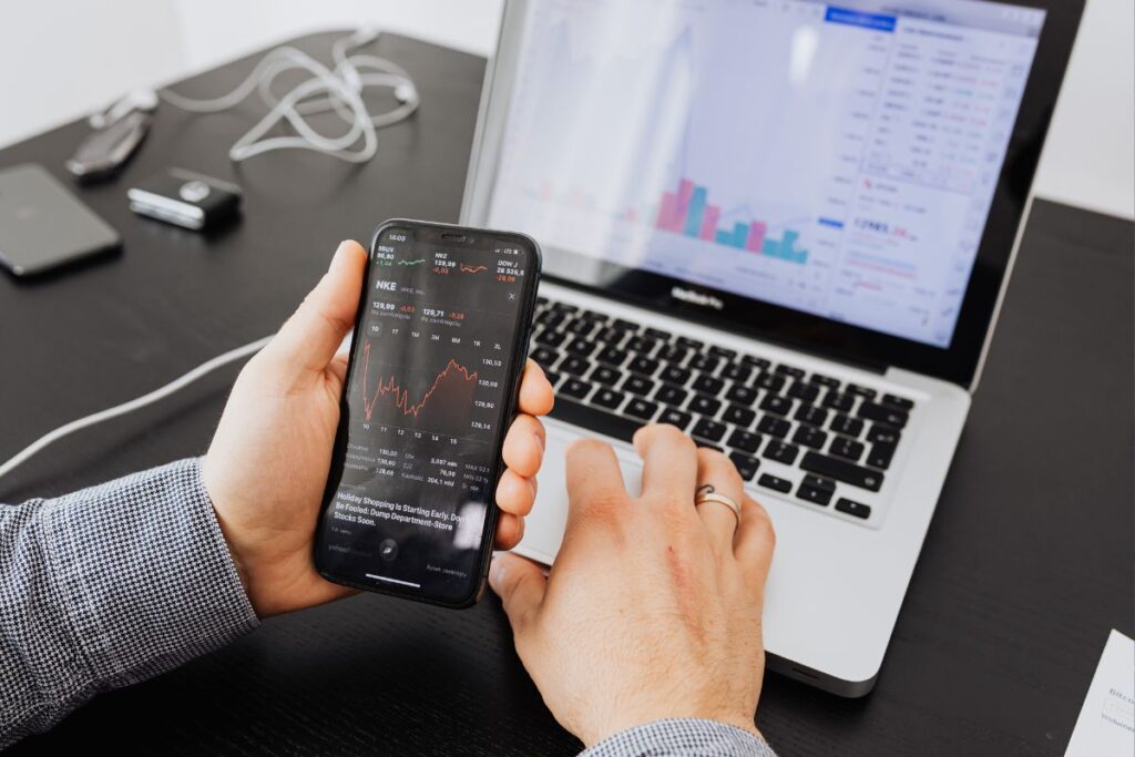 Pessoa analisando métricas financeiras no smartphone e laptop, comparando performance de diferentes de plataformas de afiliados