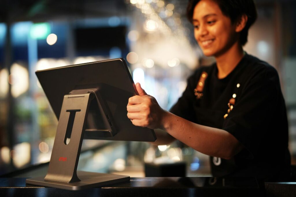 Funcionário sorrindo usando um sistema de Ponto de Venda (PDV), ilustrando a finalização da transação ou a gestão de pedidos.