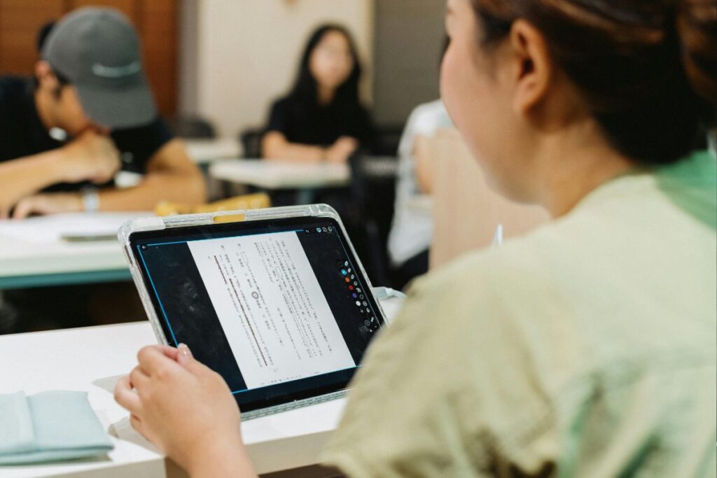 Aluna usando um tablet para ler um documento em aula, exemplificando o aprendizado para transações online ou a pesquisa para comercialização.