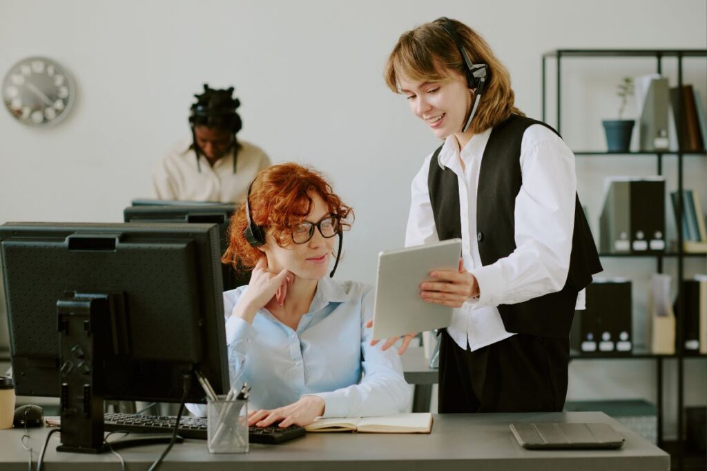 Profissionais de suporte técnico com fones de ouvido trabalhando em um escritório, dedicadas a solucionar os problemas dos clientes.