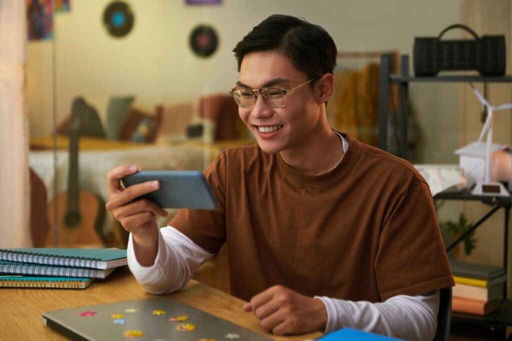 Jovem sorrindo assistindo a um vídeo no celular, encontrando a solução para sua dificuldade de aprendizado ou entretenimento.