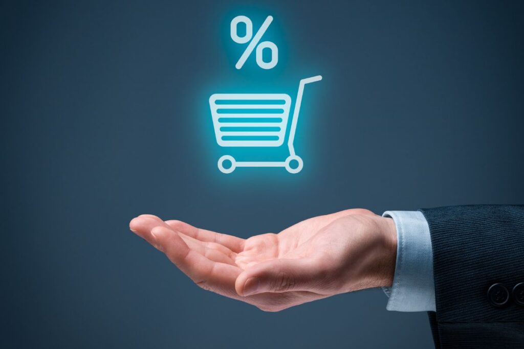 Mão segurando um ícone digital de carrinho de compras e porcentagem, representando a taxa de comissão sobre a venda de produtos.