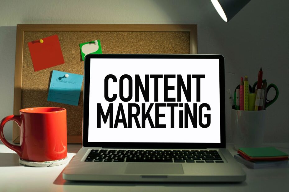 Notebook exibindo texto Content Marketing em tela branca sobre mesa de trabalho com caneca laranja e quadro de avisos ao fundo representando estratégias de marketing de conteúdo para afiliados