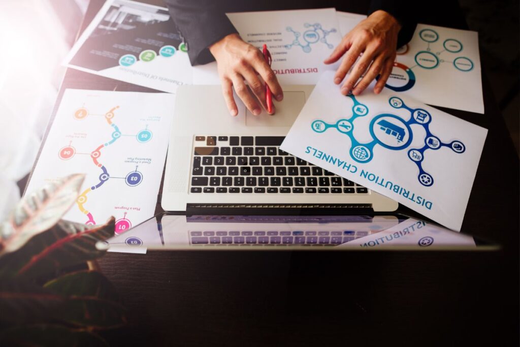 Imagem mostrando profissional trabalhando em laptop cercado por materiais de planejamento estratégico de marketing, incluindo diagramas dos 7 Ps de serviços (Product, Price, Place, Promotion, People, Physical Evidence, Process) e gráficos circulares ilustrando os 4 Ps tradicionais do marketing. A cena representa o trabalho metódico necessário para criar e promover tutoriais eficazes sobre como afiliado, demonstrando a importância de estratégia, análise de mercado e posicionamento adequado. Os documentos visíveis incluem elementos de corporate mission, situation analysis, marketing strategy e promotional mix, fundamentais para quem deseja ter sucesso promovendo ofertas digitais.