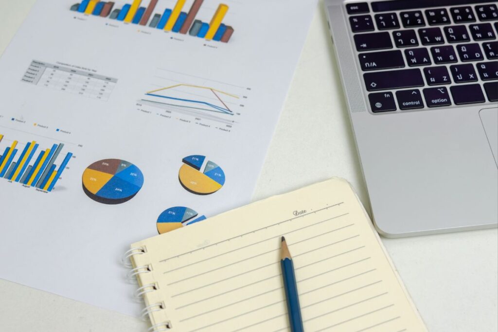 Documentos com gráficos de barras e pizza ao lado de um notebook, simbolizando a análise de dados e performance nas principais plataformas de afiliação.
