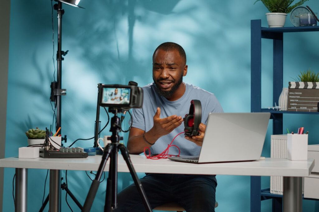 Criador de conteúdo em vídeo para afiliados gravando uma review de produto (fones de ouvido) com uma câmera profissional e iluminação.
