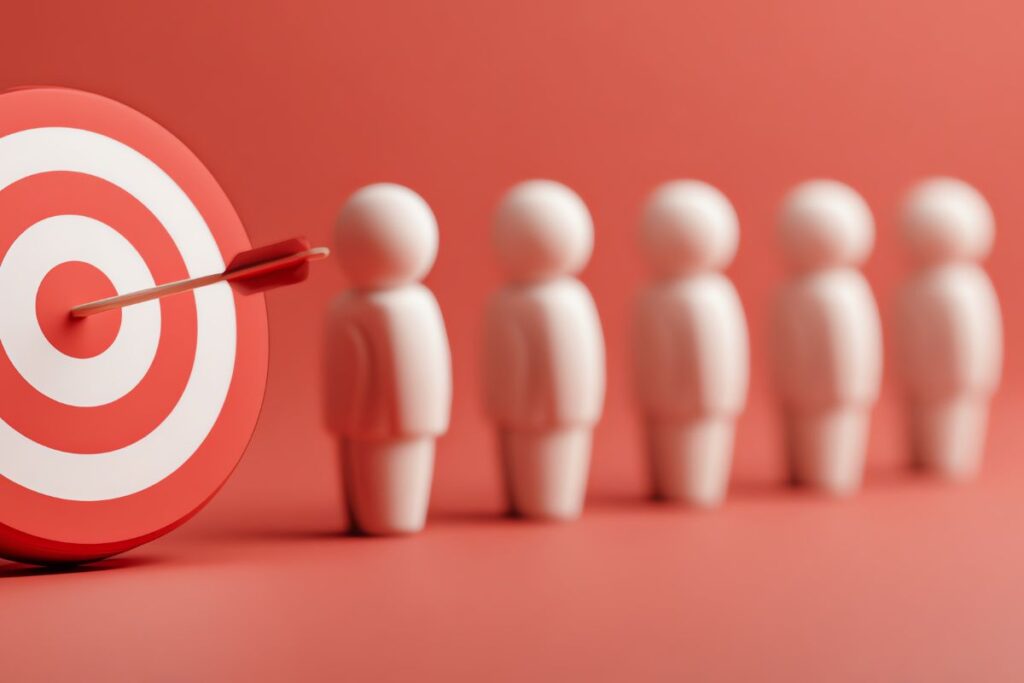 Três pessoas de palito mirando com flechas um alvo vermelho. Representa o foco no nicho e o público-alvo qualificado.